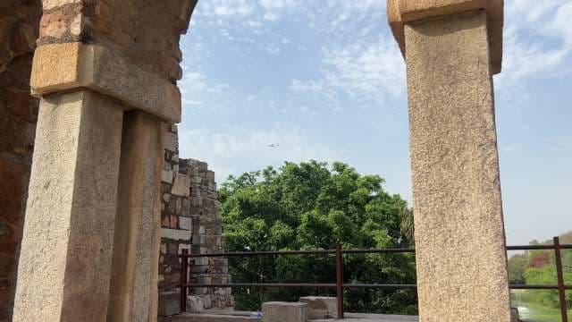 Historic Stone Archway With Lush Trees and Passing Airplane