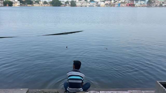 Man Relaxing By Lake With Scenic Urban View