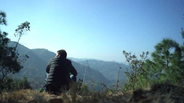 Man Sitting on Mountain Peak Overlooking Scenic Valley