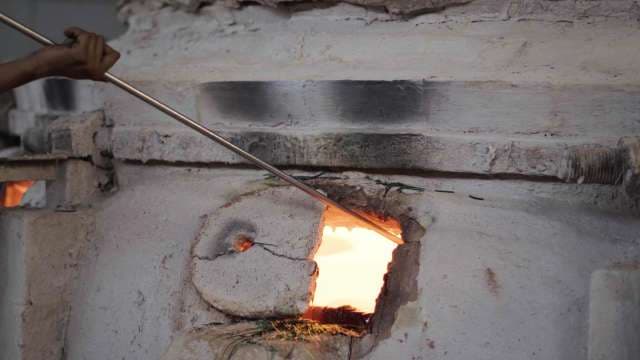 Artisan Inserting Metal Rod Into Glowing Glassblowing Furnace