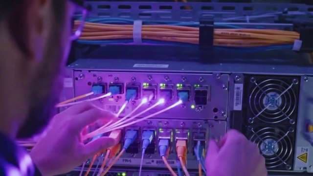 IT Technician Connecting Glowing Fiber Optic Cables in Server Room