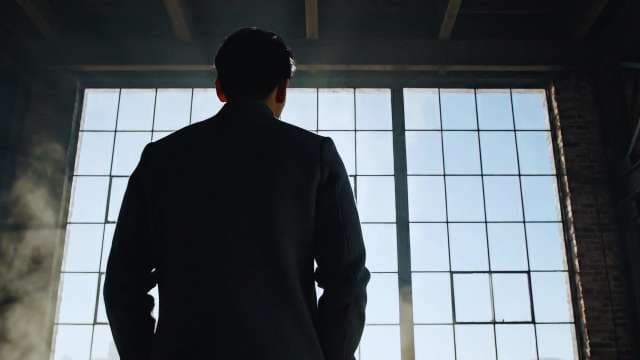 Silhouetted Businessman Standing Before Large Industrial Window