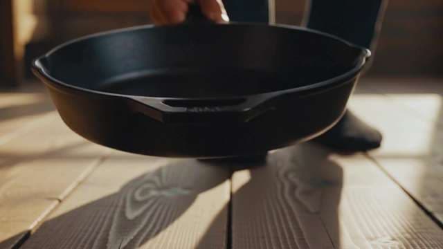 Rustic Cast Iron Skillet Being Carried Across Sunlit Wooden Floor