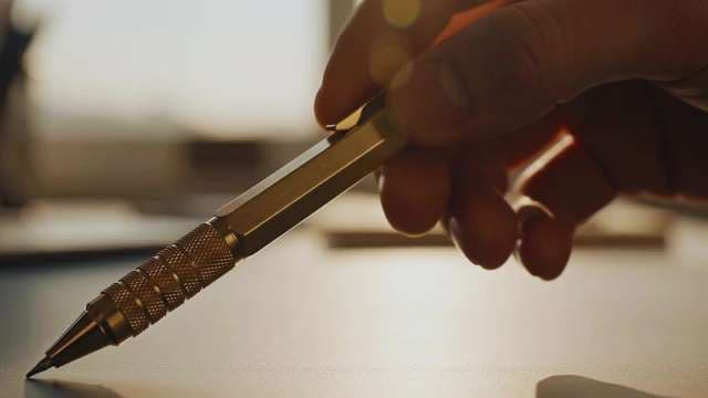 Close-up of Hand Holding Brass Pen on Office Desk