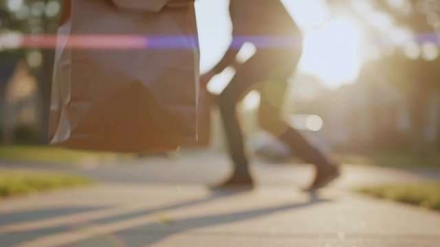 Food Delivery Person Carrying Paper Bag on Sunny Suburban Sidewalk