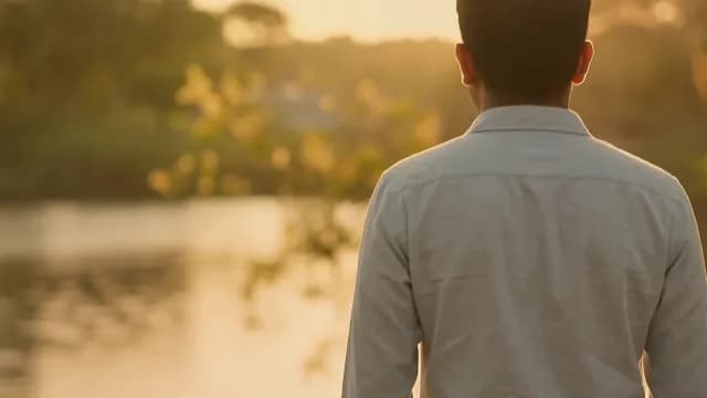 Man Standing by Calm Lake at Golden Hour Sunset