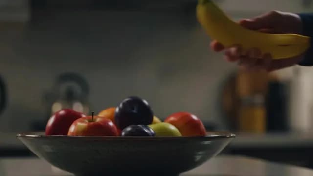 Hand Placing Fresh Banana into Ceramic Fruit Bowl in Kitchen
