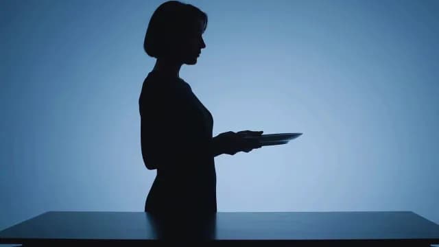 Silhouette of Woman Holding Empty Plate Against Blue Background