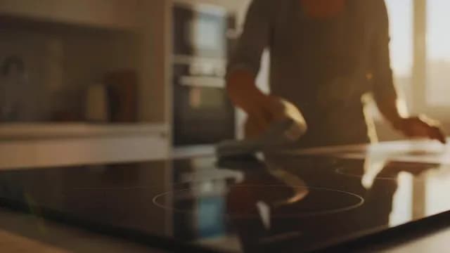 Woman Cleaning Modern Induction Cooktop in Sunlit Kitchen