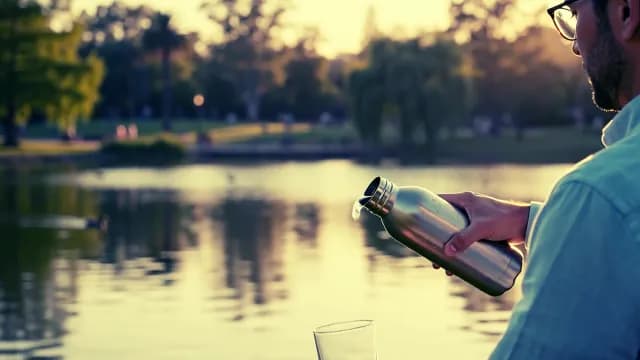 Man Pouring Water from Steel Bottle in Park at Sunset