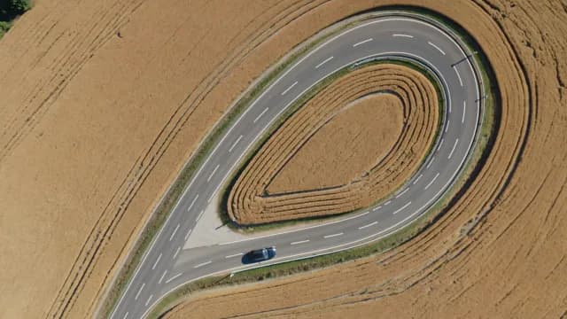 Aerial View of Car Navigating Sharp Hairpin Curve in Golden Fields