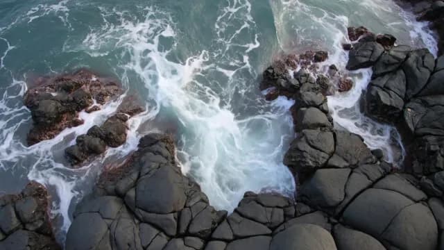 Aerial Top-Down View of Ocean Waves Crashing Against Volcanic Rocks