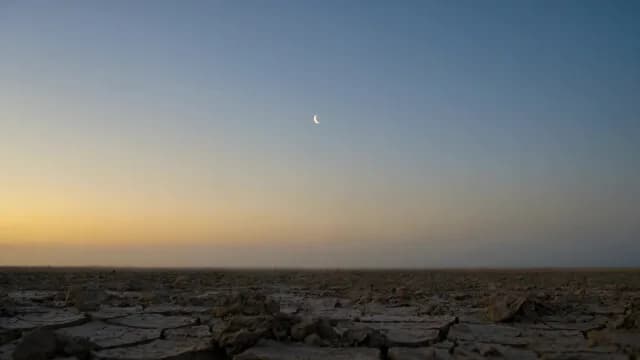 Crescent Moon Over Cracked Desert Ground at Twilight