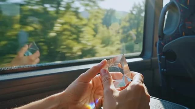 Hands Holding Glass Prism Catching Sunlight on a Moving Bus Journey