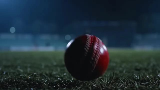 Red Cricket Ball Resting on Stadium Grass Field at Night