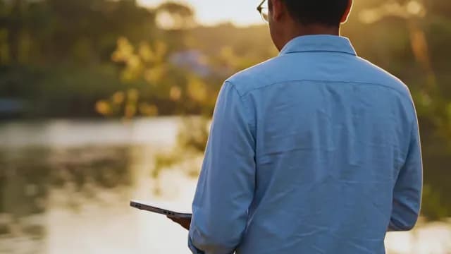 Man Working Remotely on Laptop by a Lake at Sunset
