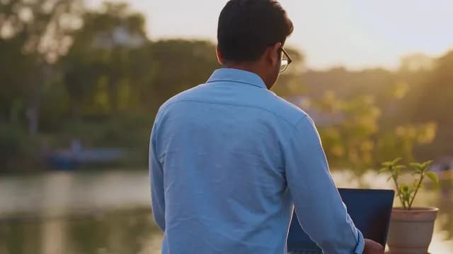 Freelancer Working on Laptop Outdoors Near River at Sunset