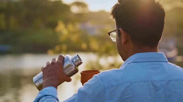 Young Man Pouring Tea from Thermos into Clay Cup at Sunset