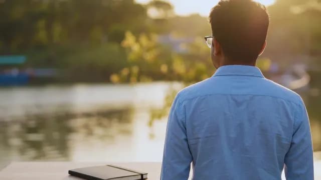 Contemplative Man Watching Sunset over Peaceful Lake during Golden Hour