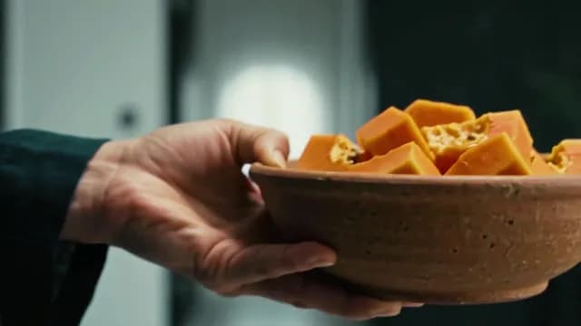 Hand Holding Rustic Clay Bowl Filled with Fresh Cubed Papaya