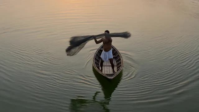 Traditional Fisherman Casting Net from Small Boat at Sunset
