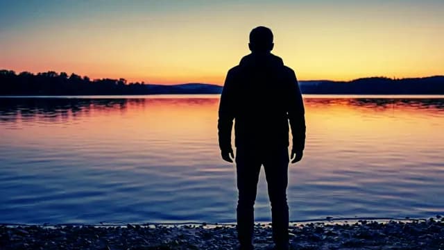 Silhouette of a Man Standing by a Lake at Sunset