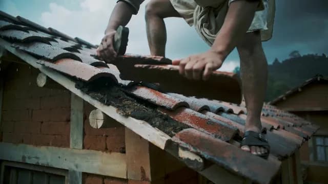 Worker Repairing Traditional Clay Tile Roof on Rural Mud Brick House