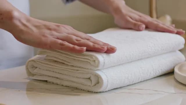 Hands Organizing Fresh White Folded Towels on Marble Countertop