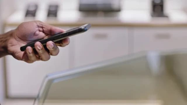 Close-up of Hand Holding Smartphone Over Glass Display Counter