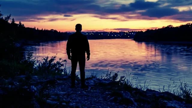 Man Silhouette Standing by River Watching Sunset Over City Lights