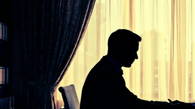 Silhouette of a Focused Businessman Working at Desk in Office