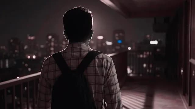 Man with Backpack Looking at City Skyline at Night