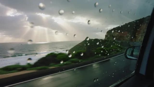 Scenic Coastal Drive with Sunbeams and Raindrops on Car Window