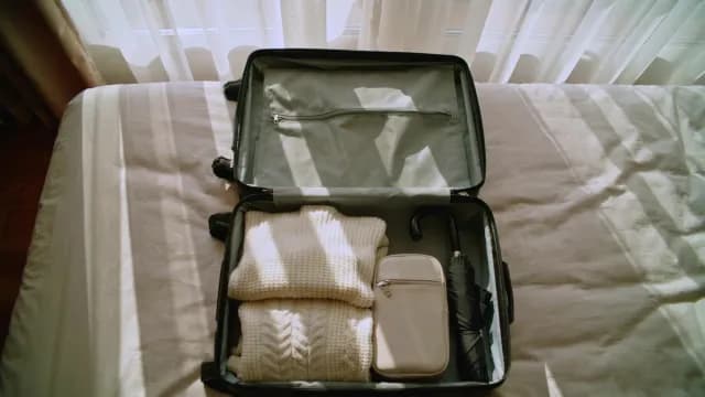 Open Suitcase Packed with Warm Sweaters and Travel Essentials on Bed
